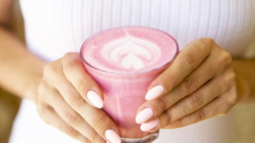 Woman's hands holding a glass of pink beetroot latte with froth on top