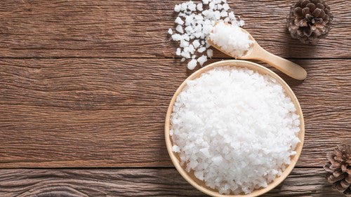 Wooden bowl and small wooden scoop filled with white epsom bath salts
