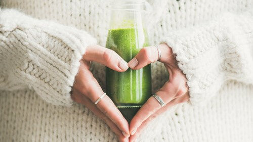 woman's hands making a heart shape and holding a green smoothie