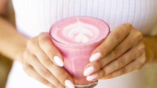 Woman's hands holding a glass of pink beetroot latte with froth on top  