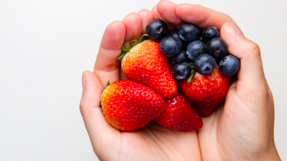 person holding handful of blueberries and strawberries