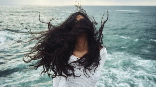 woman with long dark hair blown in her face in front of the sea