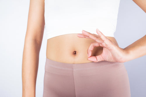 Woman with a slim torso doing OK sign against bare tummy.