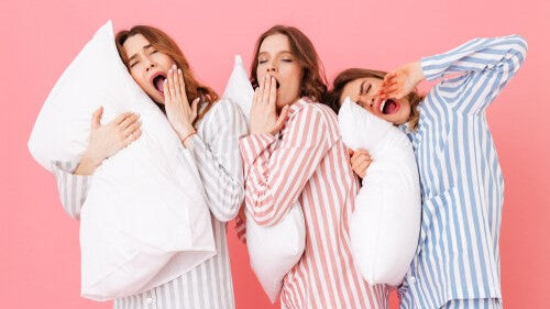 3  young women in striped pyjamas holding pillows and yawning