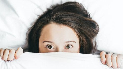 Woman with dark hair peeking out from under a white duvet set